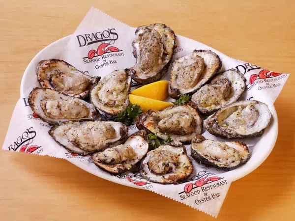 Grilled oysters on a white plate with lemon wedges, served on branded paper from Drago's Seafood Restaurant.