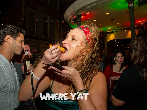 Woman in red headband eating fried food at lively nighttime party with people drinking and socializing.
