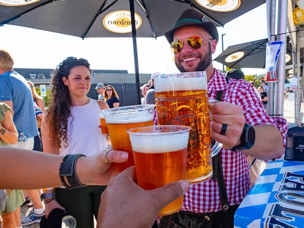 Group of people clinking large beer mugs and cups at an outdoor festival under branded umbrellas