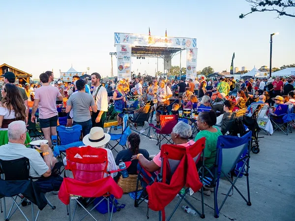 Crowd enjoying an outdoor music festival with people sitting on chairs and socializing near the stage at sunset.