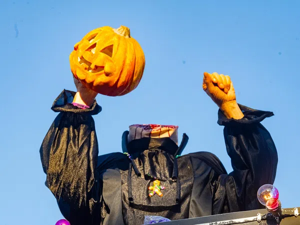 Headless Halloween figure in black costume holding a carved pumpkin against a clear blue sky.