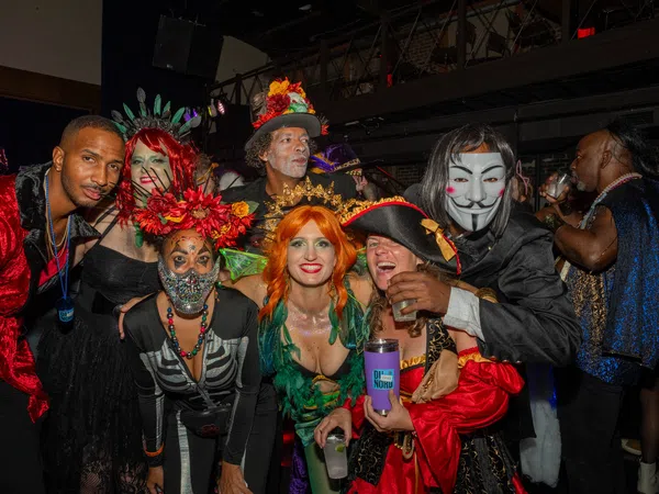 Group of adults in colorful and creative costumes posing indoors at a lively Halloween or costume party.