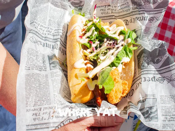 Fresh fried fish sandwich with lettuce and sauce served in newspaper-style wrapping held by a person.