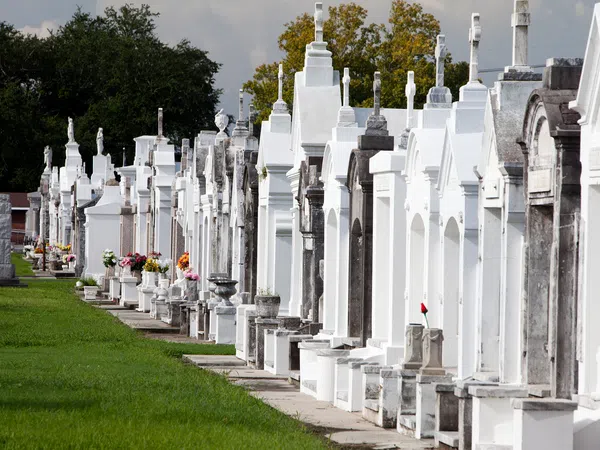 Row of white and gray above-ground tombs with flowers in a cemetery on a sunny day.