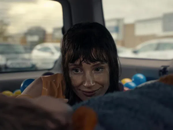 Woman with wet hair smiling inside a car filled with colorful plastic balls, looking at someone out of focus.