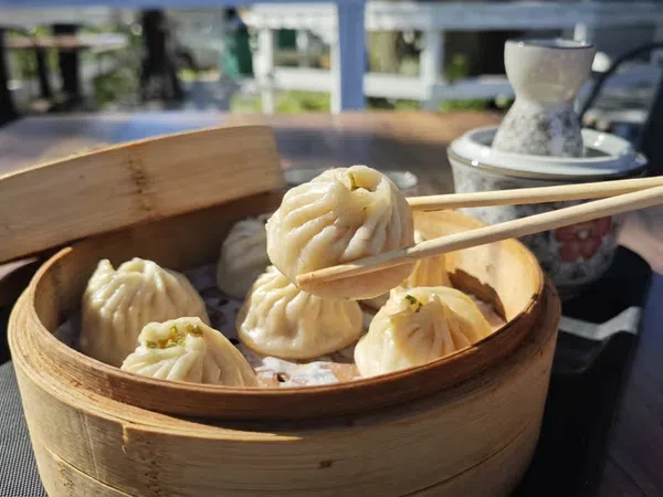Chopsticks picking up a steamed dumpling from a bamboo basket on a wooden table outdoors