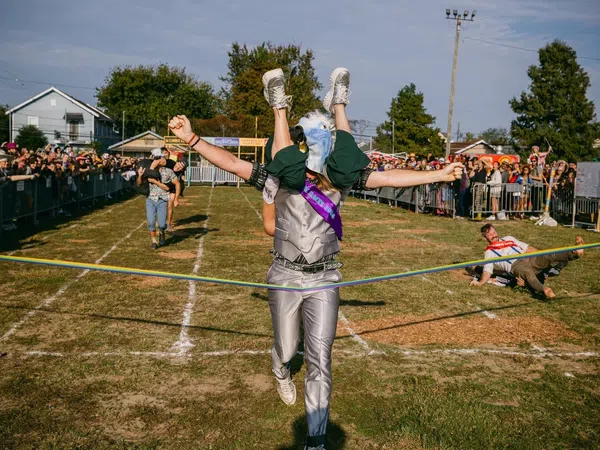 Person in eagle costume winning a race while carrying another runner across the finish line at outdoor event.