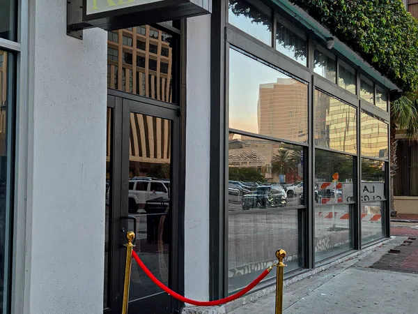 Entrance to KIRA with black door, red velvet rope, gold stanchions, and green ivy on urban building facade.