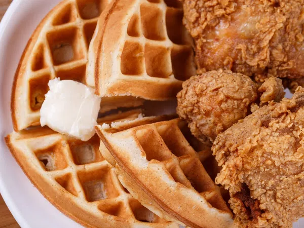 Crispy fried chicken pieces served with golden waffles and a dollop of melting butter on a white plate.