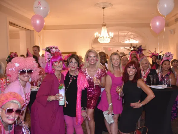 Group of women dressed in pink and black at an indoor party with balloons and drinks celebrating together.
