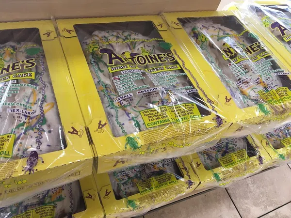 Stacked boxes of Antoine's King Cake with yellow packaging, showcasing traditional Mardi Gras colors and design.
