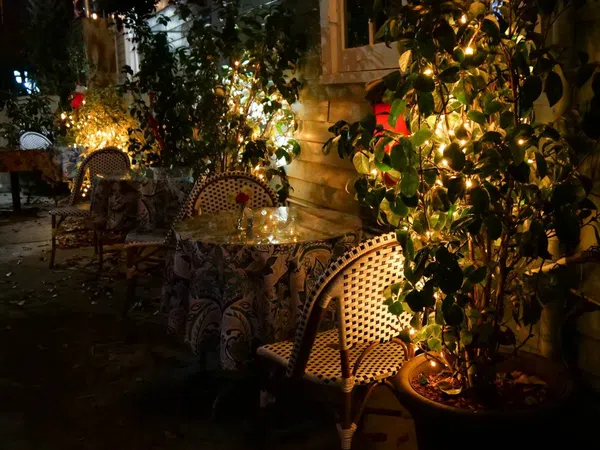 Cozy outdoor cafe seating with patterned chairs and tables lit by warm string lights at night.