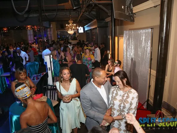 Crowded lively indoor party with guests socializing, dressed in formal and cocktail attire under chandeliers.