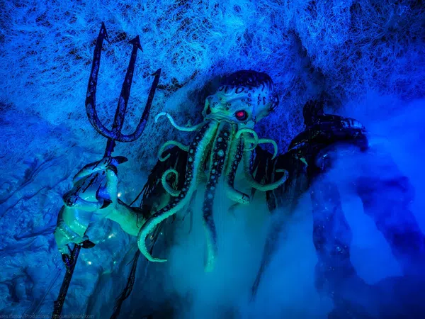 Cthulhu figure with glowing red eyes holding a trident amidst blue fog and web-like textures underwater.