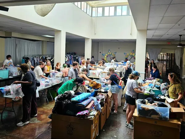 Volunteers sorting and organizing clothing donations in a large, well-lit community center with boxes and racks of clothes.