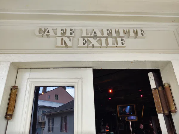 Entrance of Cafe Lafitte in Exile with white wooden doors and reflective glass showing buildings outside.