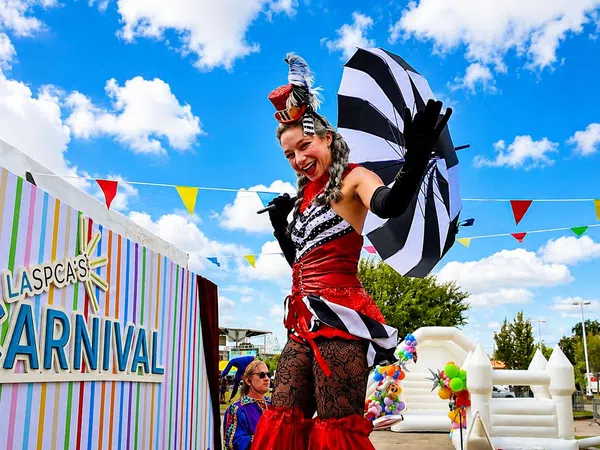Performers in colorful carnival costumes entertain at LASPCA's outdoor community carnival event under a bright blue sky.