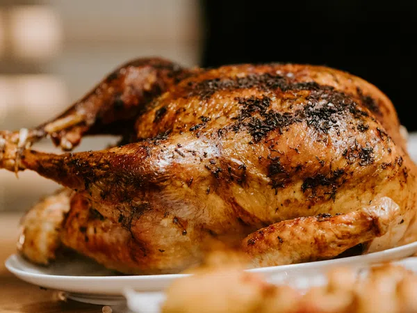 Golden-brown roasted whole chicken with herbs on a white plate ready to serve.