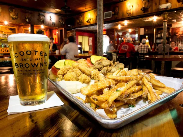 Fried seafood platter with fries and a cold beer glass on a wooden table in a cozy bar setting.