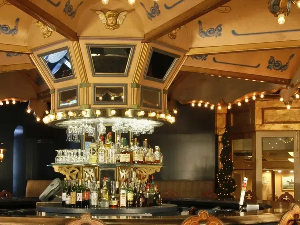Elegant vintage bar interior with ornate ceiling, lights, central liquor display, and wooden chairs under warm lighting.
