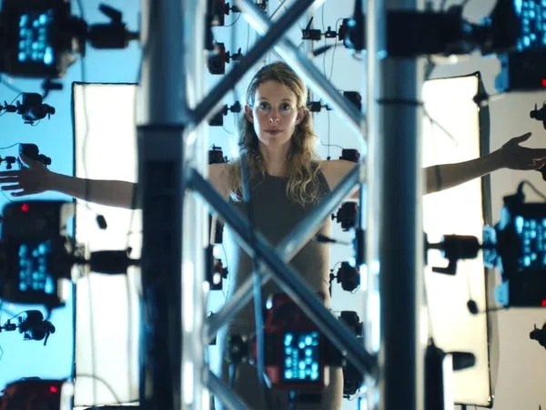 Woman standing inside a 3D scanning rig with arms outstretched surrounded by cameras and lighting panels.