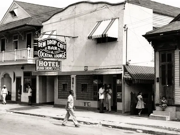 Black and white street scene with Dew Drop Cafe bar, cocktail lounge, hotel, and people walking and standing outside.