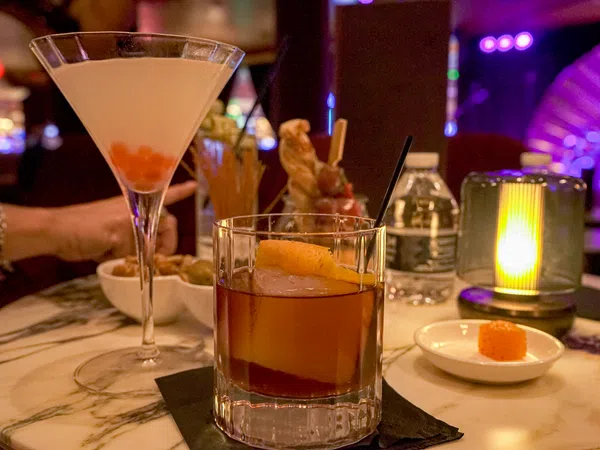Cocktails served on a marble table with dim lighting and a water bottle in a cozy bar setting.