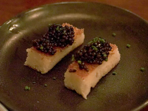 Two rectangular pieces of toasted bread topped with black caviar and garnished with chopped chives on a dark plate