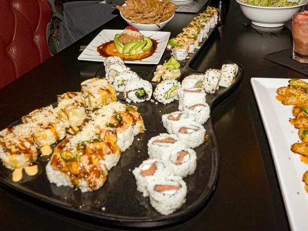 Assorted sushi rolls with sauces and garnishes served on a black platter and white plates on a dark table.