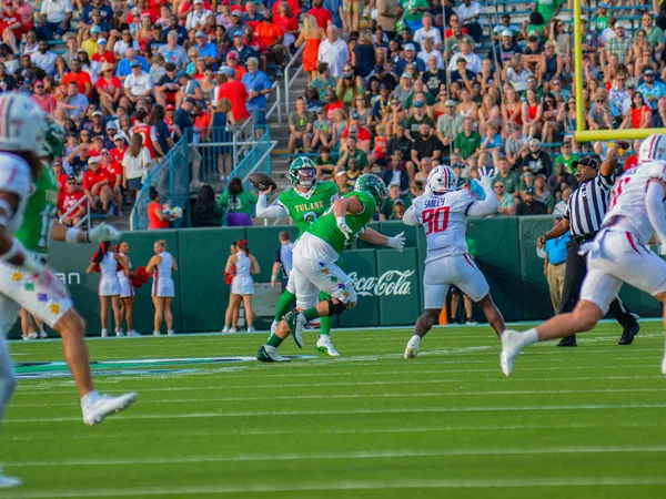 Tulane quarterback prepares to throw under pressure from defenders with crowd and cheerleaders in background