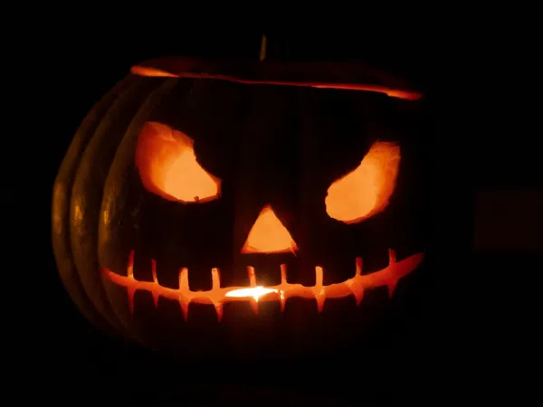 Glowing Halloween jack-o'-lantern with menacing eyes and stitched mouth carved in pumpkin in darkness