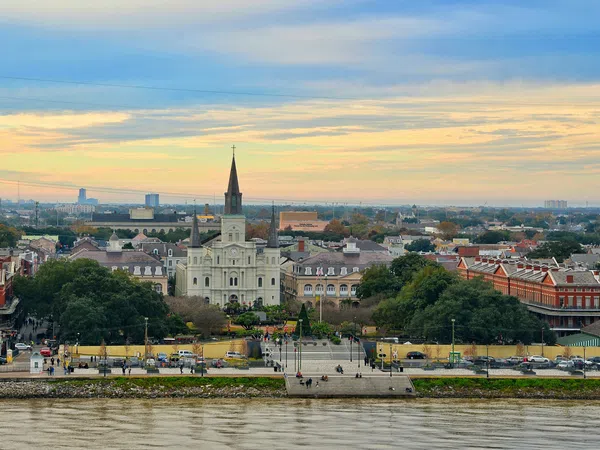 Stunning view of St. Louis Cathedral and Jackson Square with the Mississippi River in the foreground at sunset.