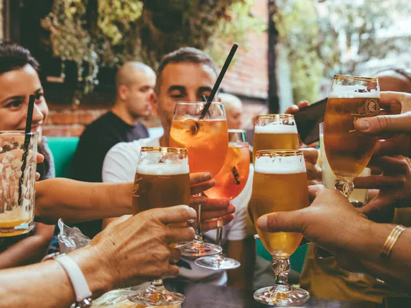Group of friends clinking glasses with beer and cocktails at an outdoor social gathering.