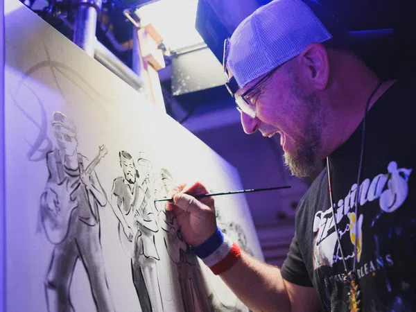Artist in cap painting a monochrome group portrait on canvas in a studio with focused expression