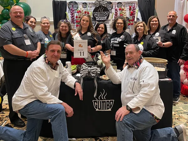 Group of people posing at Gumbo Season Fest booth with festive decorations and promotional materials.