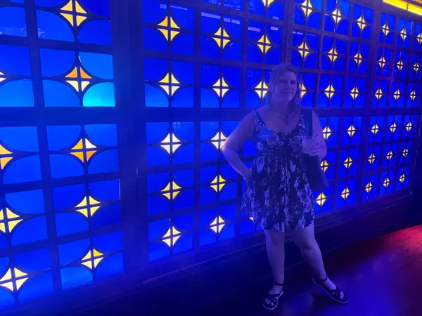 Woman in a floral dress standing in front of a vibrant blue and yellow patterned illuminated wall.