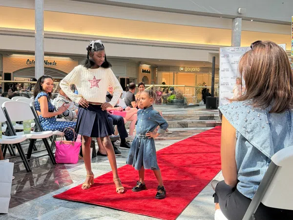 Two young models confidently posing on a red carpet runway during a fashion event in a shopping mall.