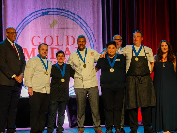 Group of chefs and officials posing with medals on stage at Gold Medal Plate culinary competition event.