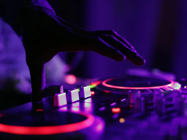 Close-up of a DJ's hand adjusting controls on a colorful illuminated mixer in a dark room.