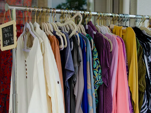 Clothing rack with diverse shirts and sweaters in various colors, with overlaid chalkboard sign showing sale details.