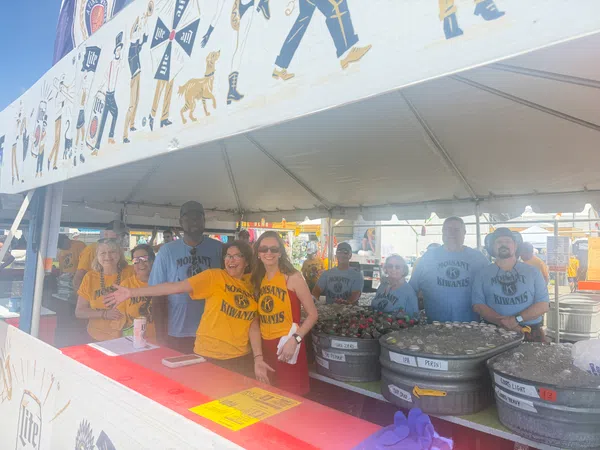 Group of Molsaint Kiwanis volunteers smiling and serving drinks under a festival tent with beer tubs.