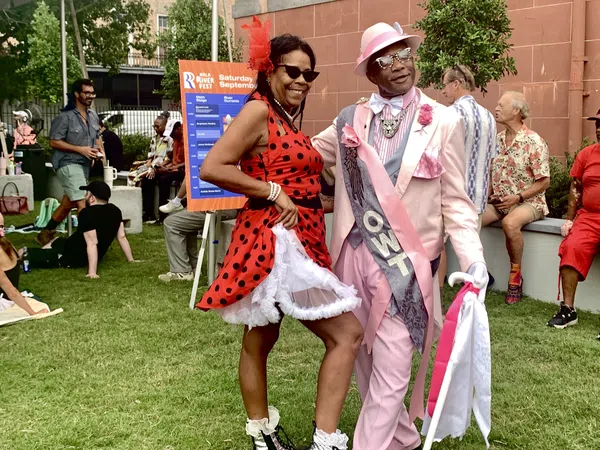 Couple dressed in vibrant retro outfits enjoying an outdoor festival on a sunny day with people relaxing nearby