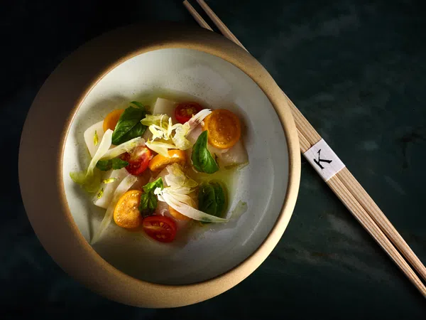 Elegant bowl of fresh vegetable salad with cherry tomatoes, greens, and chopsticks on dark surface.