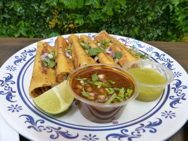 Plate of golden taquitos garnished with cilantro and onions, served with lime wedges and two dipping sauces.