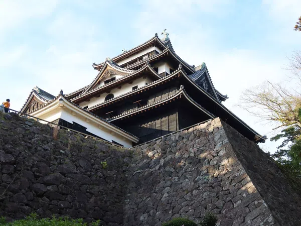 Traditional Japanese castle with multi-tiered roofs atop large stone walls under a clear sky.