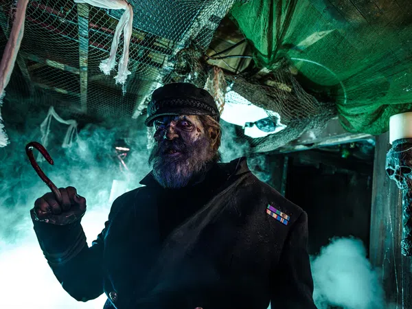 Dark haunted captain with a hook hand and eerie blue lighting in a spooky, fog-filled ship interior.