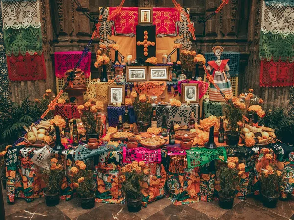 Traditional Mexican Day of the Dead altar decorated with marigolds, papel picado, photos, skeletons, and food offerings.