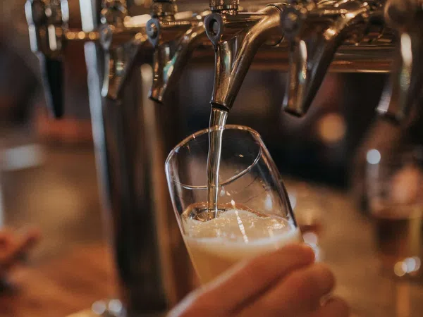 Beer being poured from a tap into a tilted glass at a bar with blurred background.