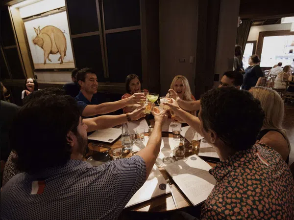 Group of friends raising glasses for a toast around a restaurant table with menus and drinks.