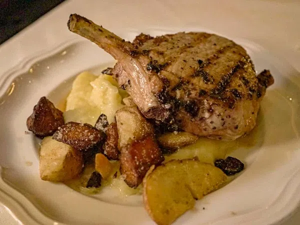 Grilled pork chop with mashed potatoes and roasted root vegetables on a white plate.